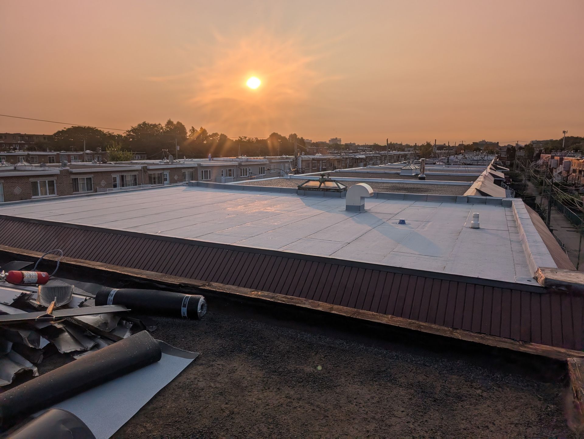 Coucher de soleil sur un toit plat recouvert d'une bâche blanche et jonché de matériaux de construction.
