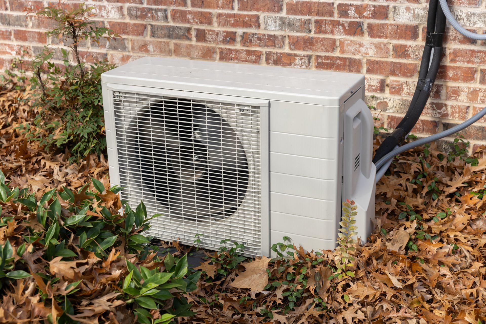 Outdoor HVAC unit against a brick wall, surrounded by fallen leaves