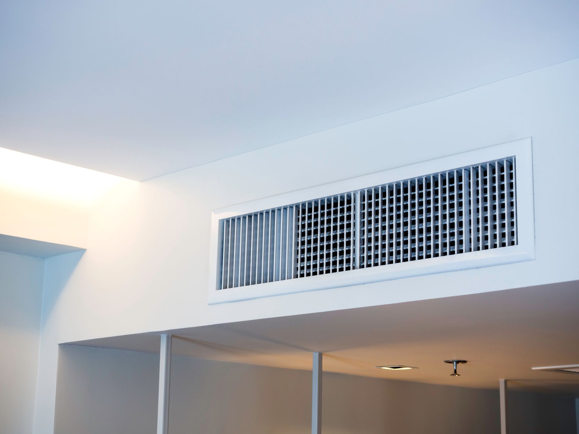 Indoor wall vent above a doorway in a white room, with ceiling lights and vents visible