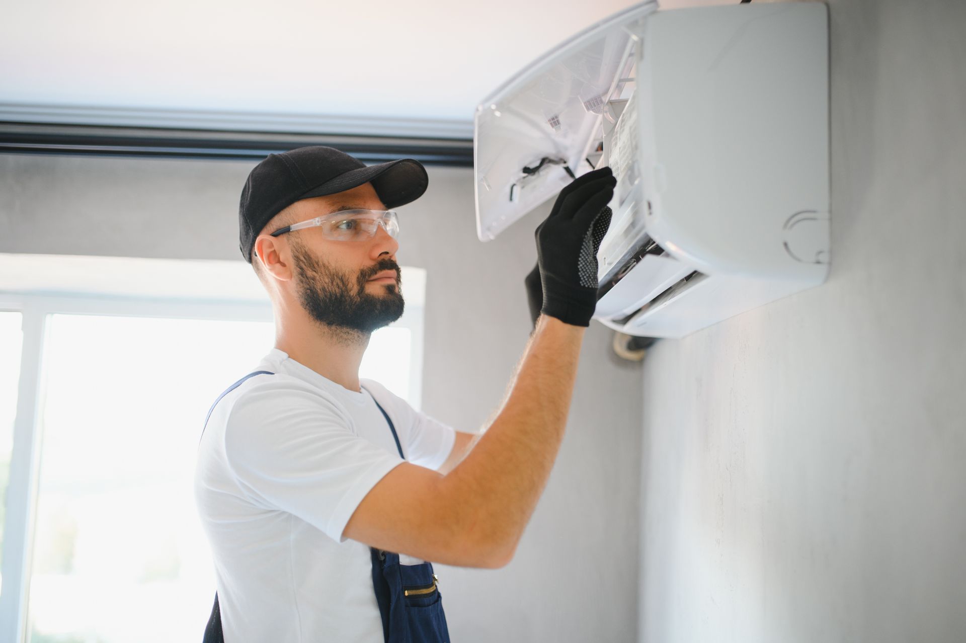 Technician repairing a wall-mounted air conditioner indoors with tools and gloves