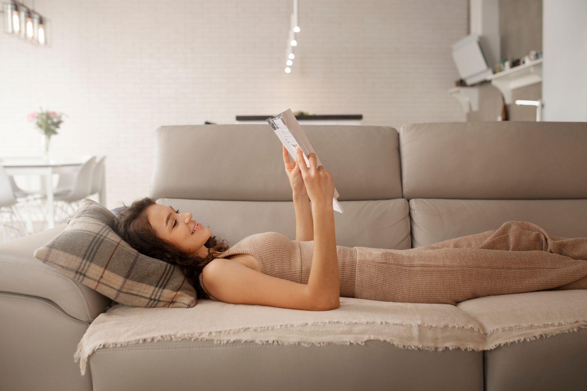 Woman lying on a couch reading a book in a bright living room