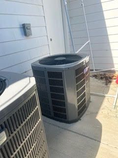 Two air conditioners are sitting on the sidewalk in front of a house.