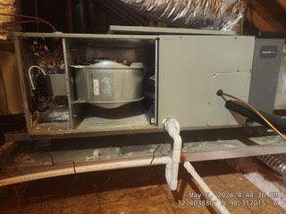 An air conditioner is sitting on top of a wooden table in an attic.