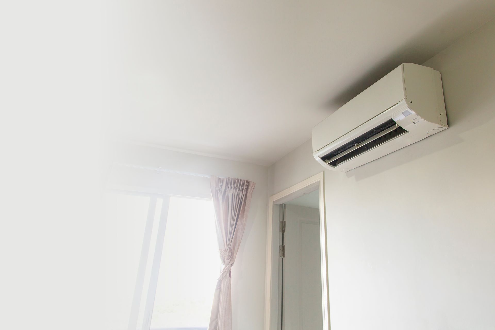A white air conditioner is hanging from the ceiling in a room next to a window.