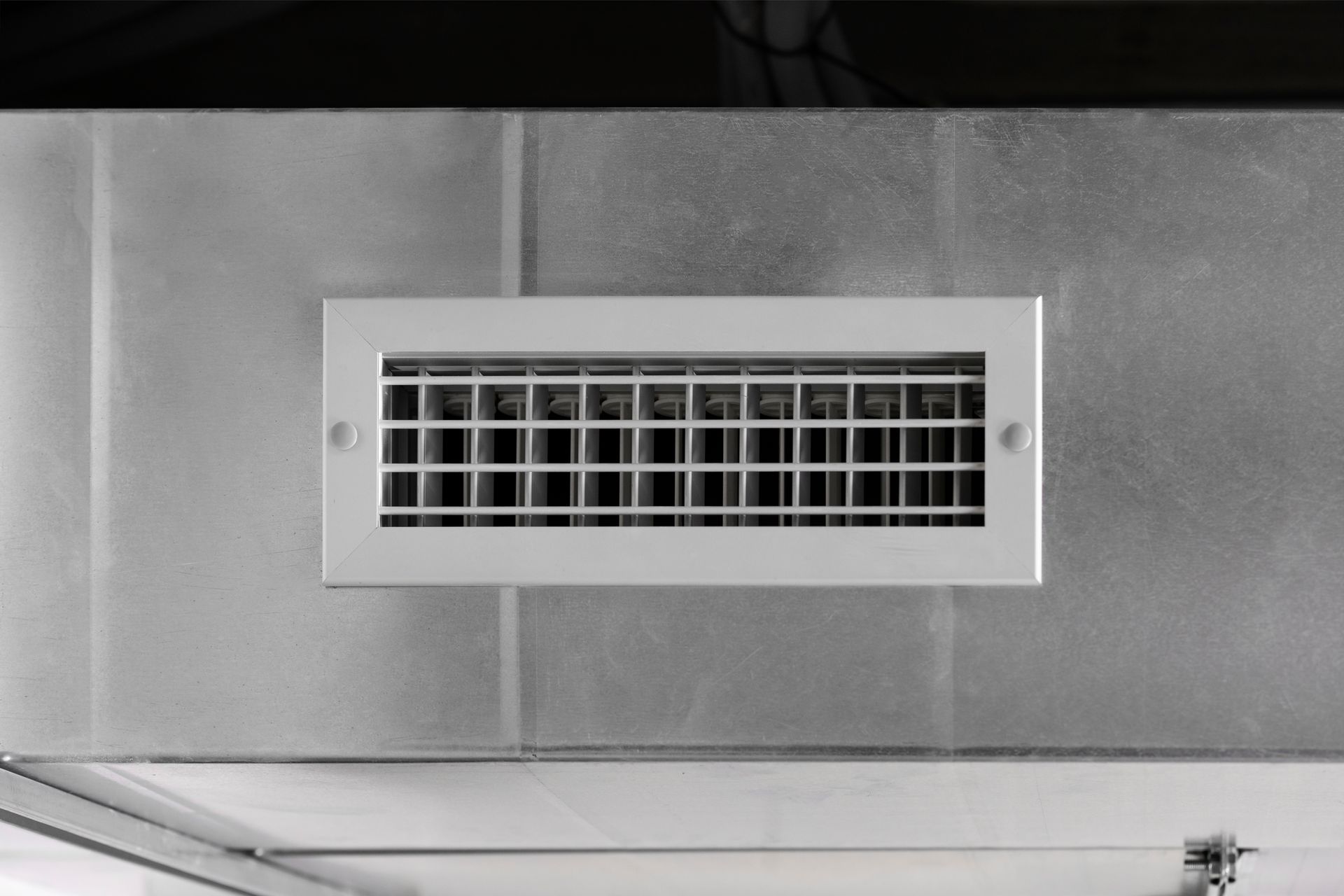 A white air vent is mounted to a metal wall.