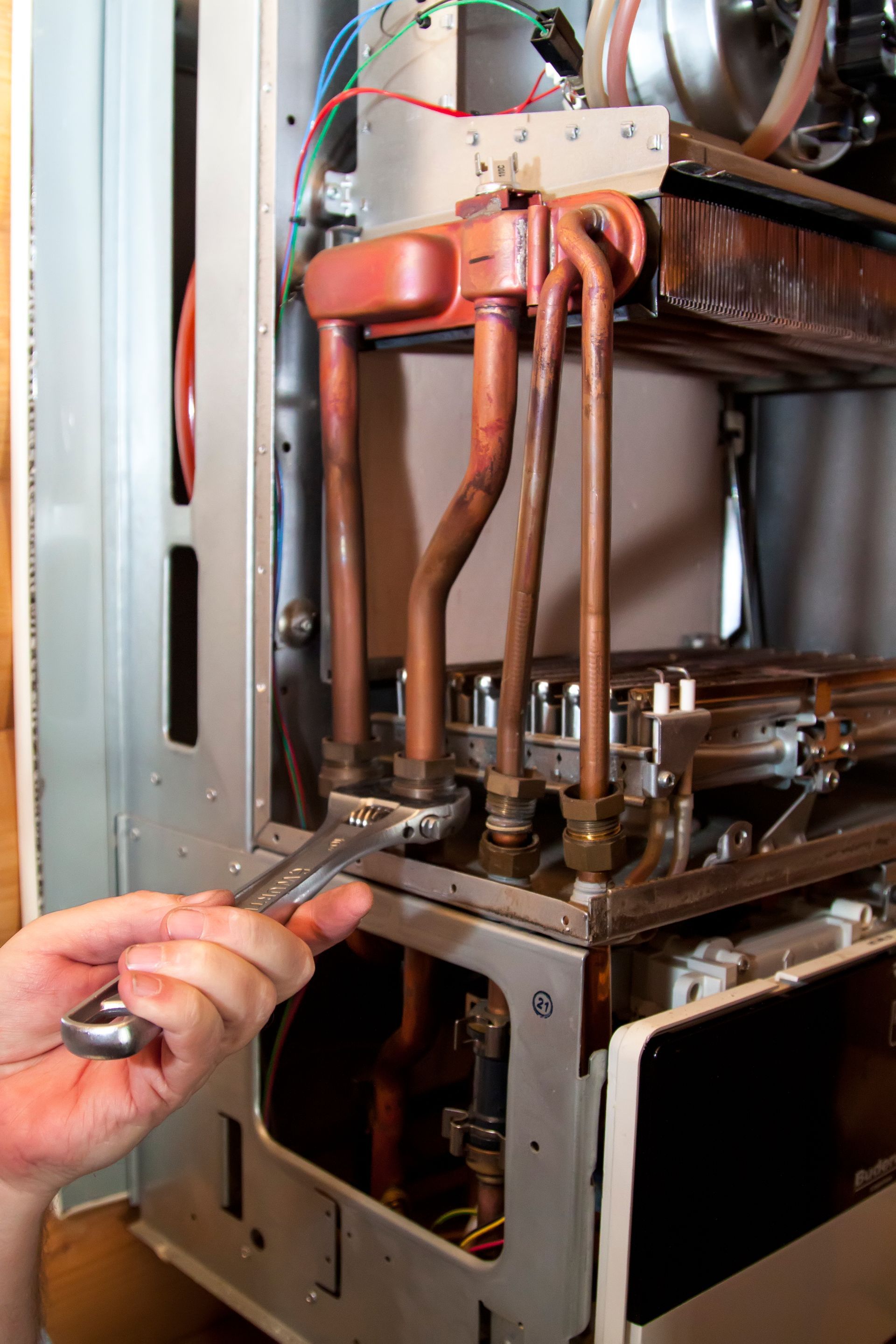 A person is working on a boiler with a wrench.