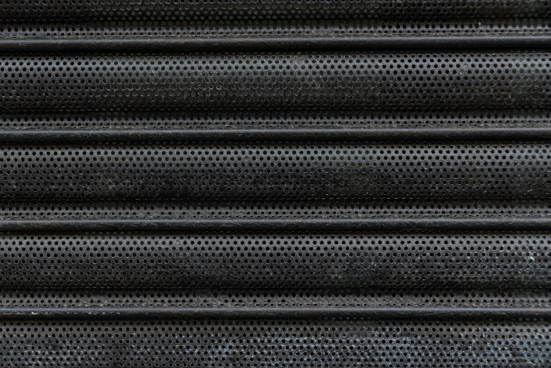 A close up of a black metal shutter with holes in it.