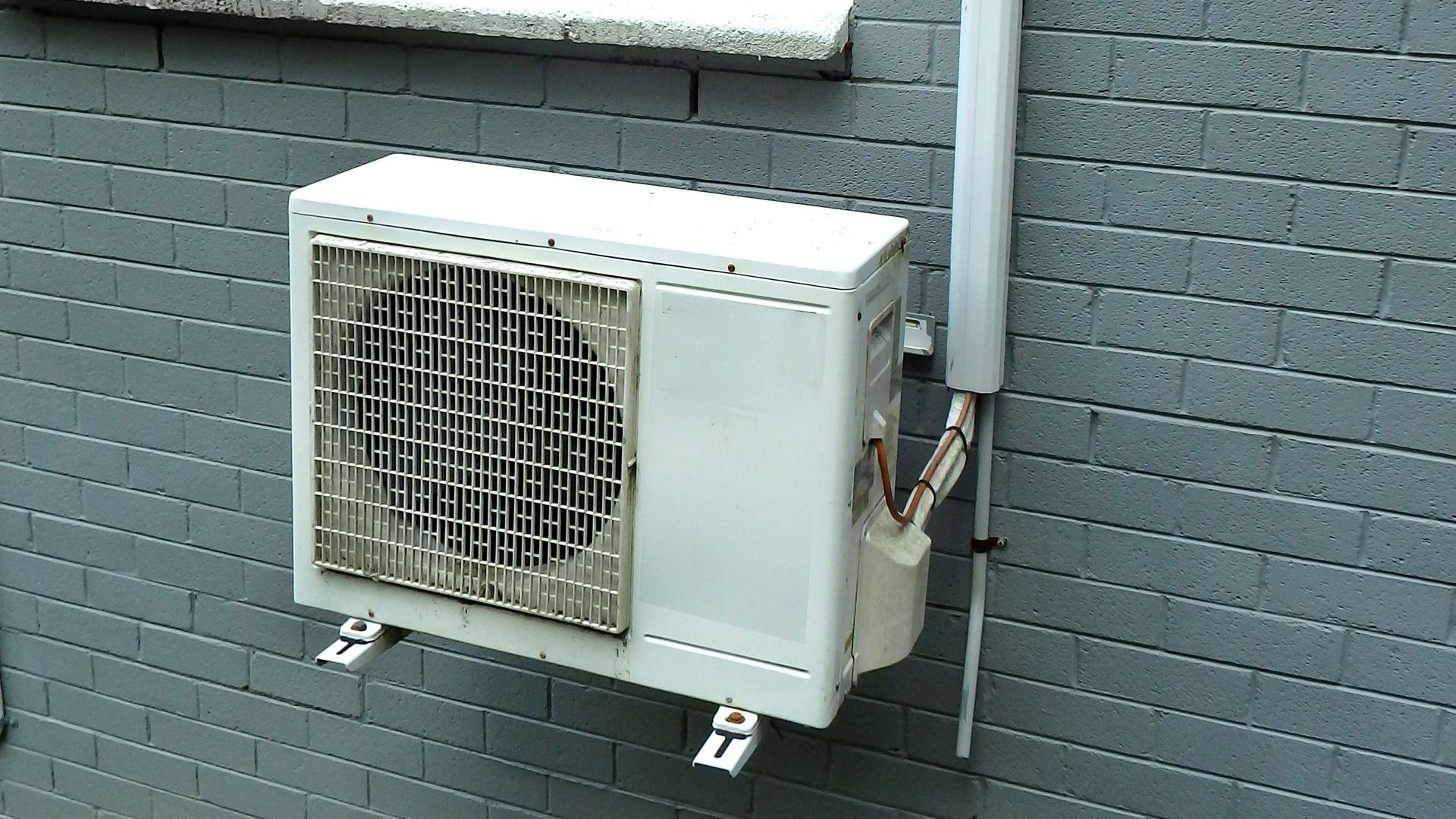 A white air conditioner is mounted to a brick wall