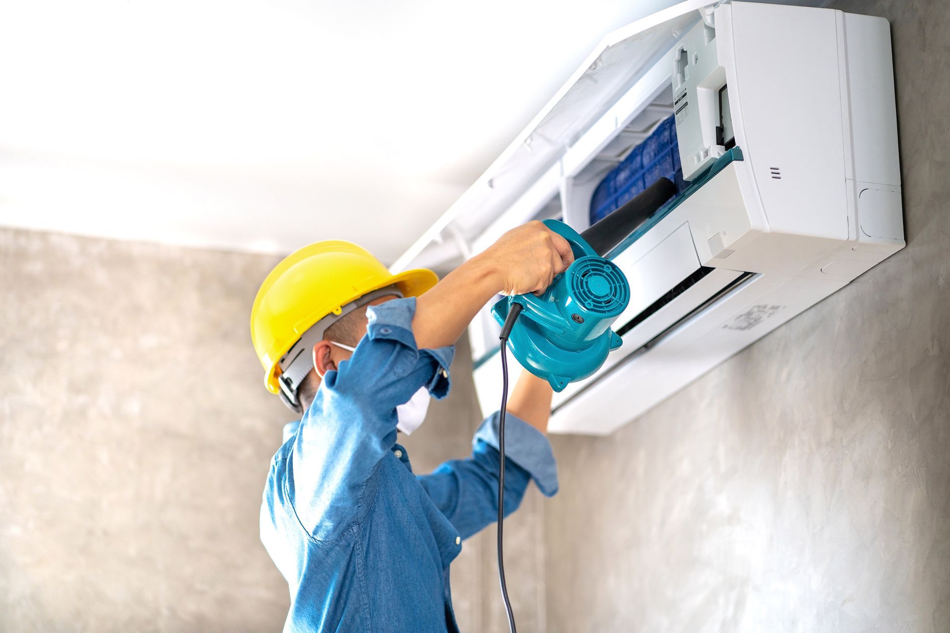A man wearing a hard hat and mask is working on an air conditioner.