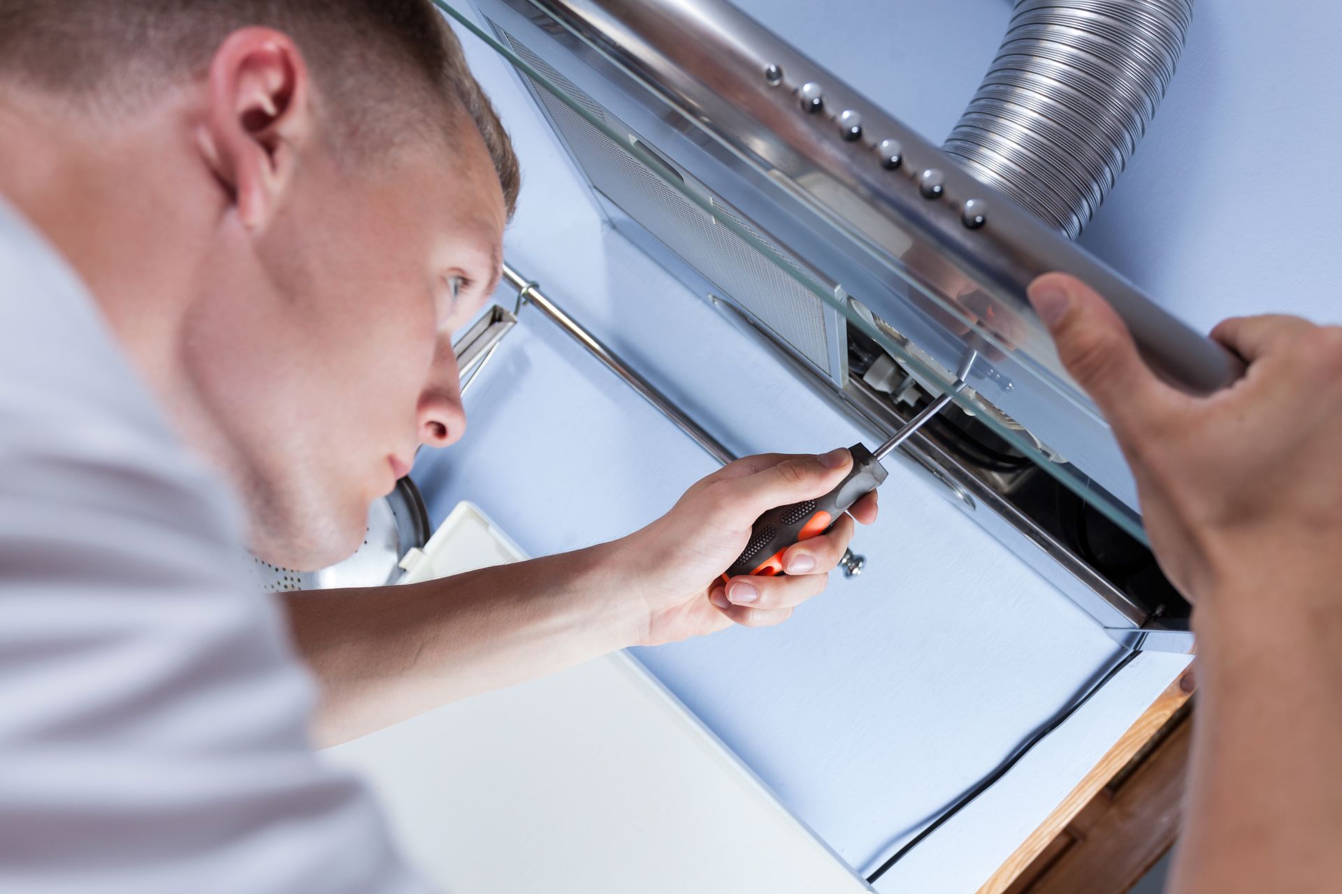 A man is fixing a kitchen hood with a screwdriver.