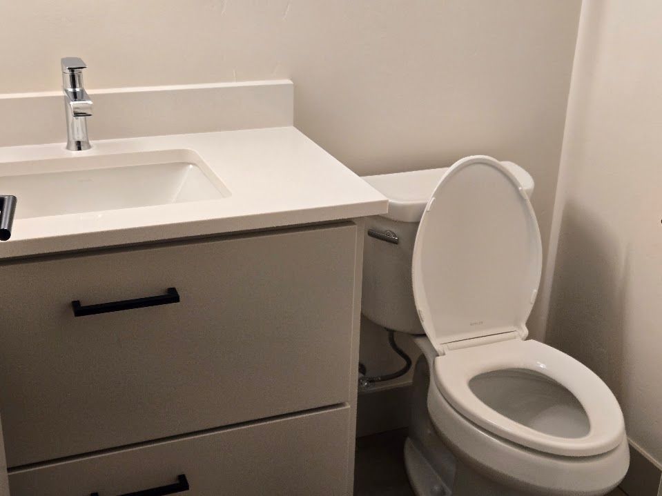 A modern bathroom with a light-colored vanity, a white countertop sink with a silver faucet, and a white toilet.