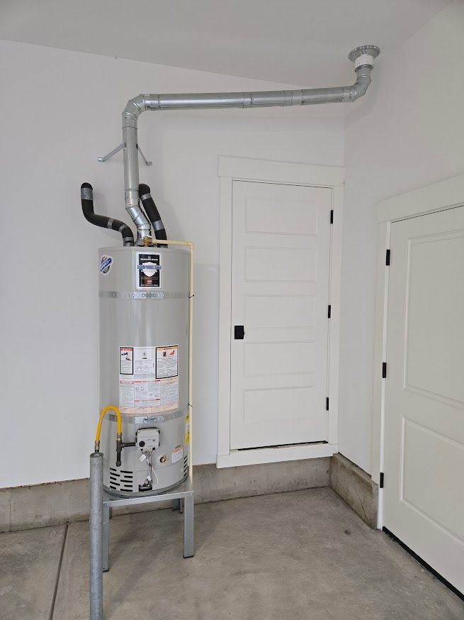 A grey water heater on a metal stand in a garage corner with a metal exhaust pipe connected to the ceiling.