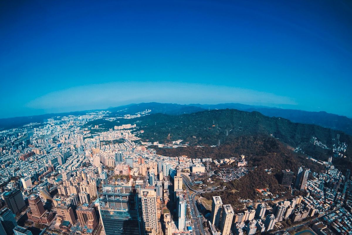 從空中俯瞰一座城市，高樓林立，山脈環繞，藍天白雲。