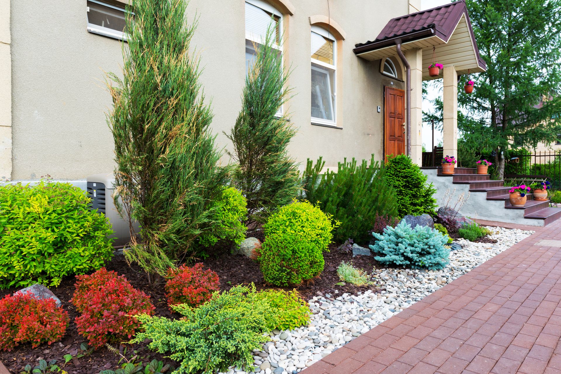 Landscaped front yard with colorful shrubs, white stones, and a brick walkway beside a house.