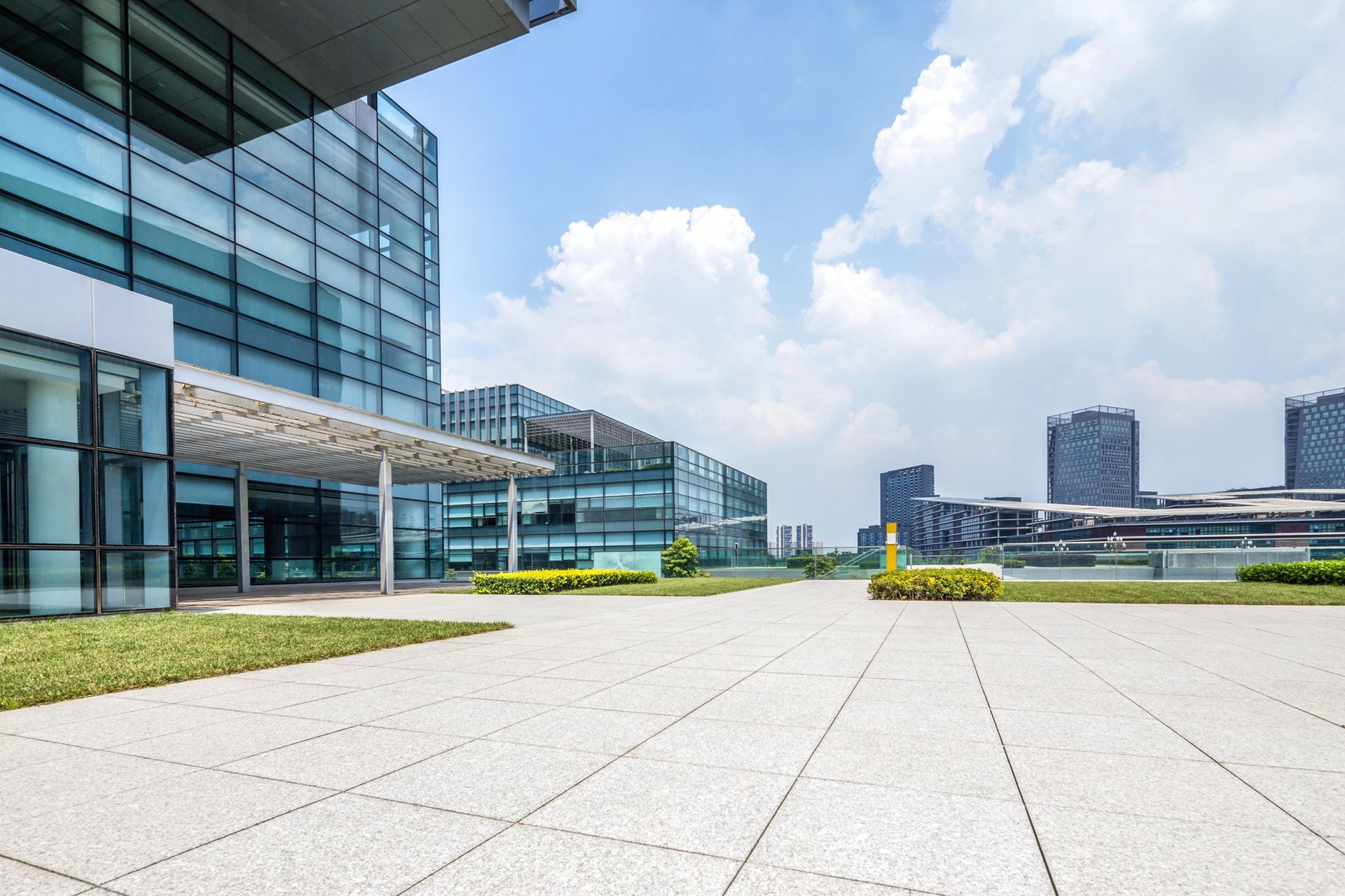 Modern glass buildings with a concrete plaza and a blue sky.