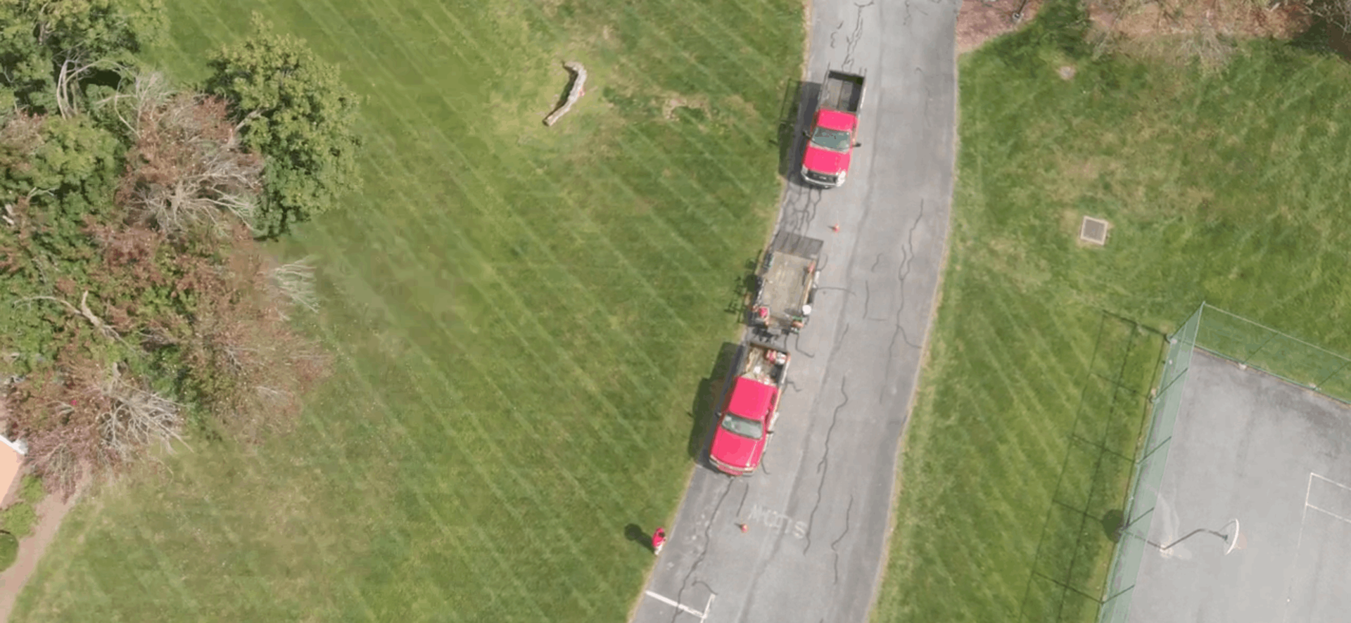 Aerial view of two red cars parked along a narrow road beside a grassy field.