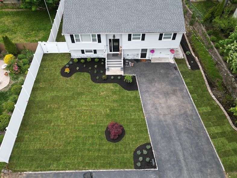 Aerial view of a white house with a gray roof, paved driveway, and landscaped front lawn.