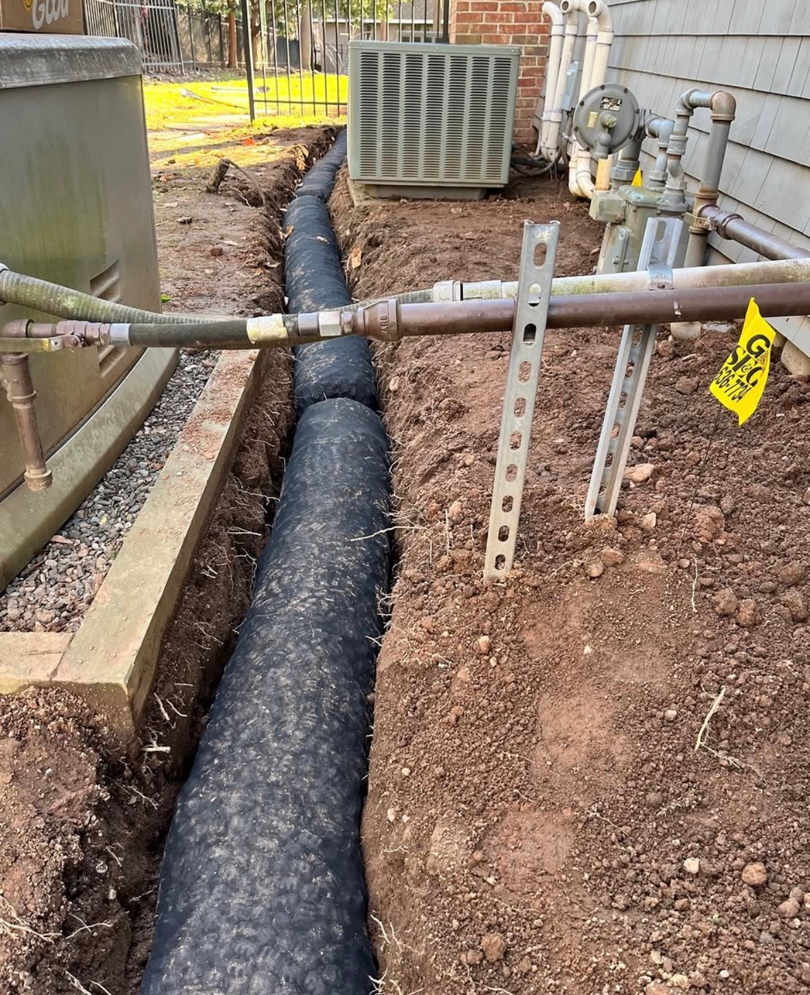 Trenched yard with black pipe, gas meter, and utility pipes beside a house