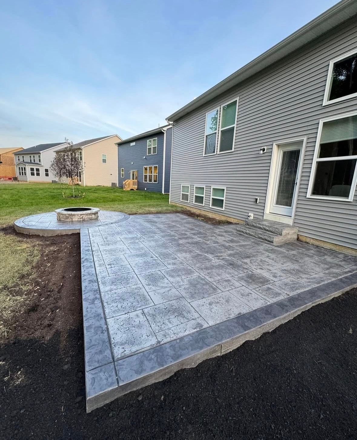 Gray paver patio beside a townhouse, with a circular fire pit and fresh landscaping