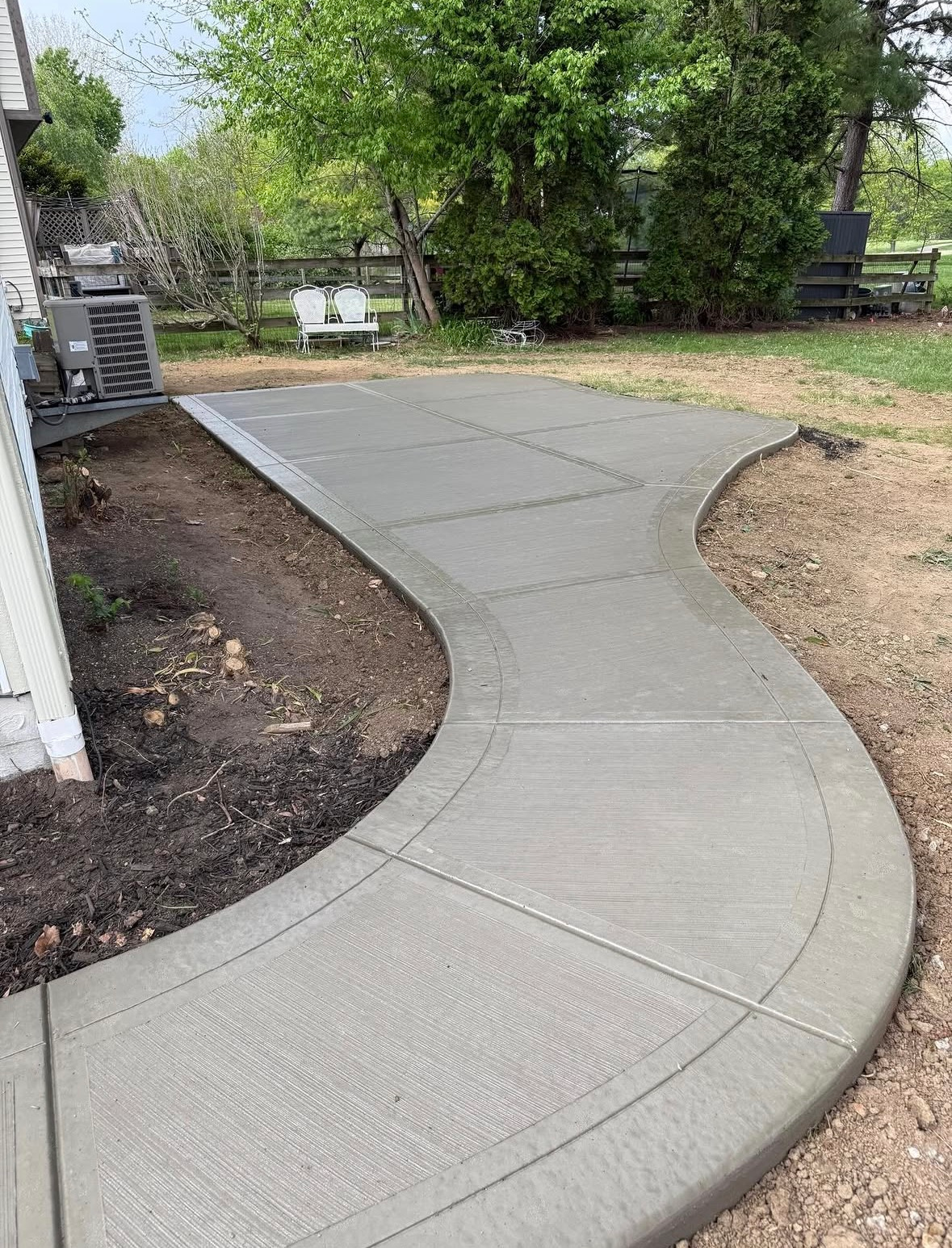 Curved concrete walkway through a yard with fresh landscaping on both sides