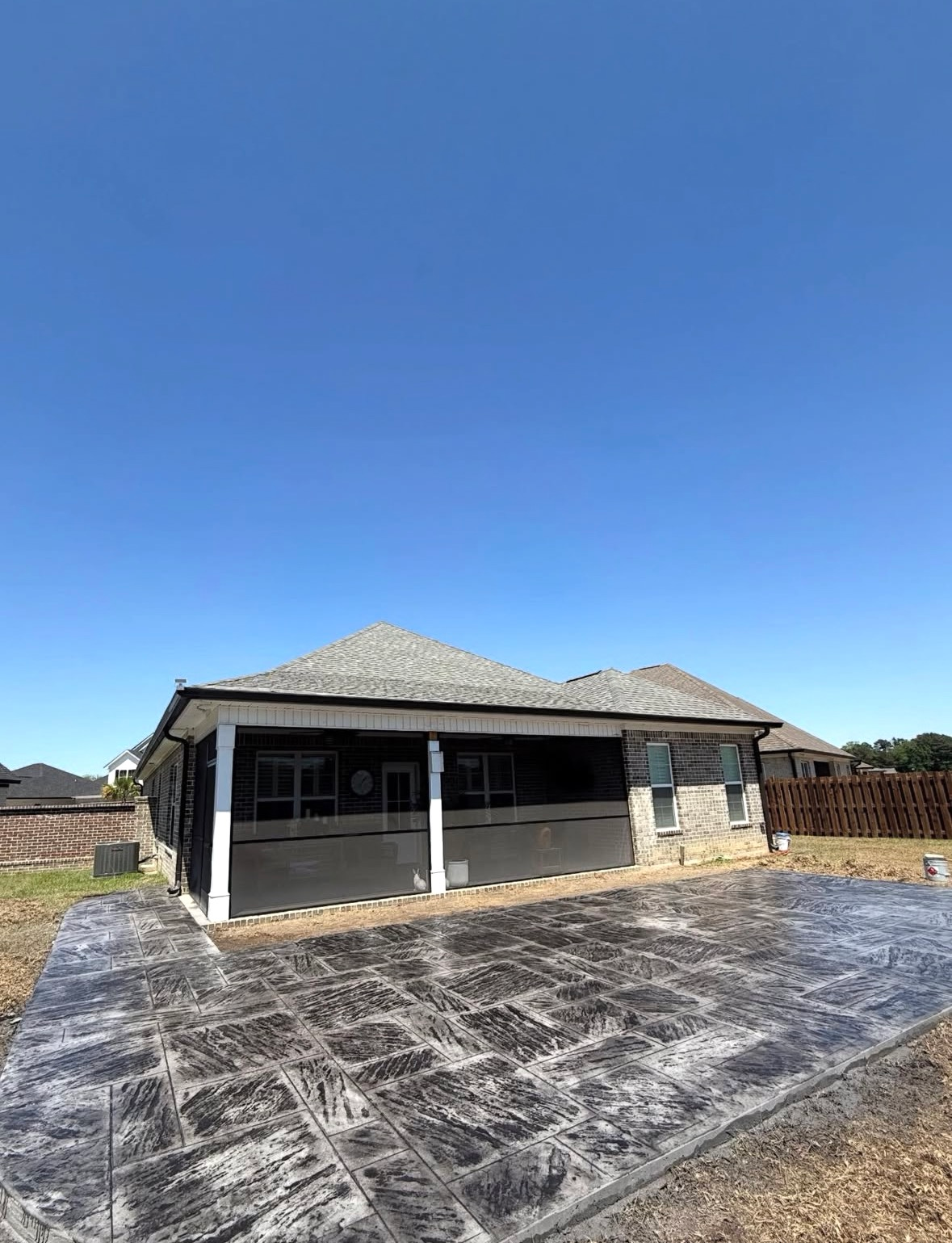 Single-story house under construction with a gray roof, white columns, and a dirt driveway under a clear blue sky