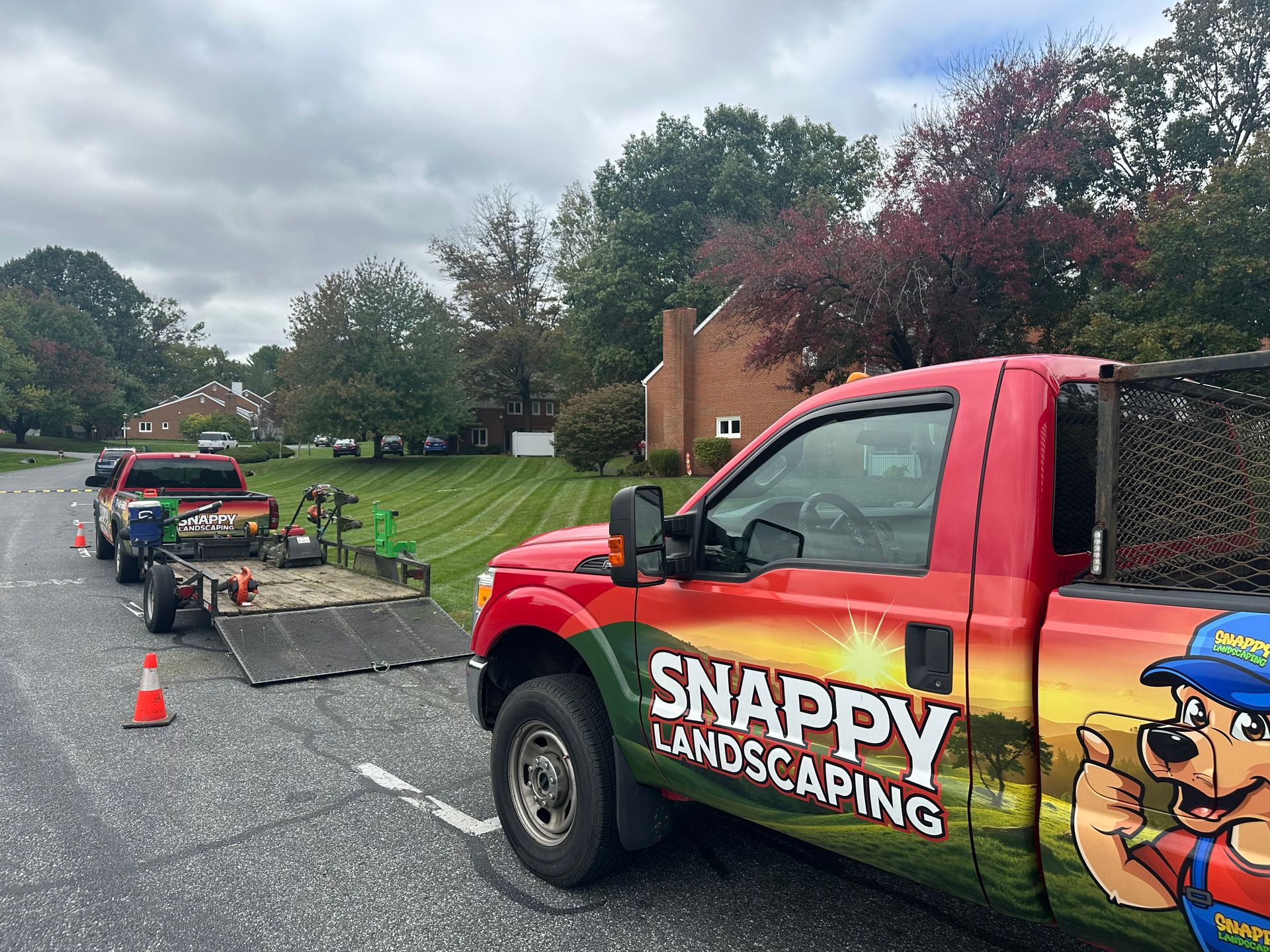 Commercial / HOA Services SNAPPY Landscaping truck parked by roadside work area with cones and equipment trailer on a cloudy day