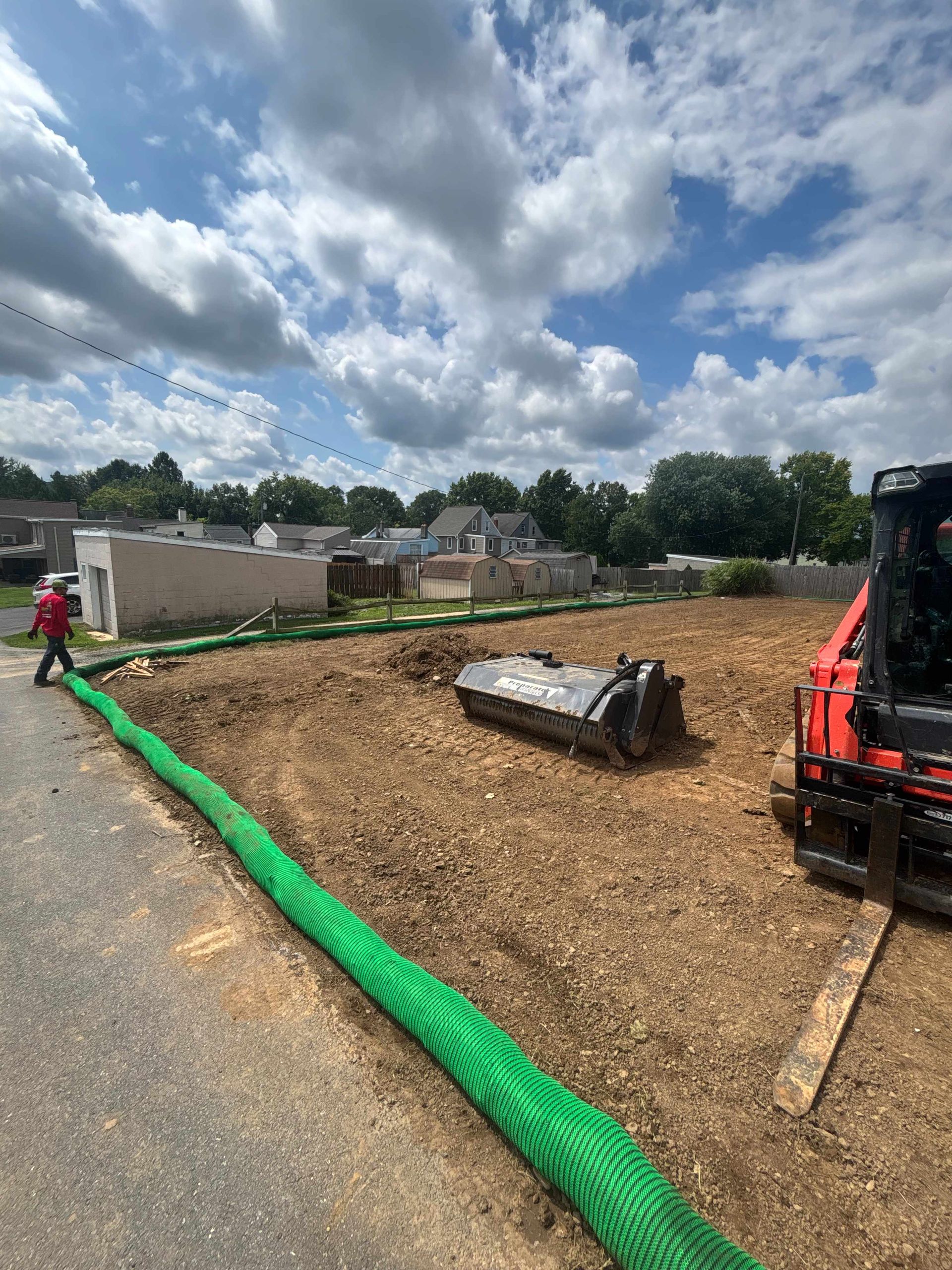 Roadwork site with orange machinery, mulch-covered ground, green erosion barrier, and cloudy sky