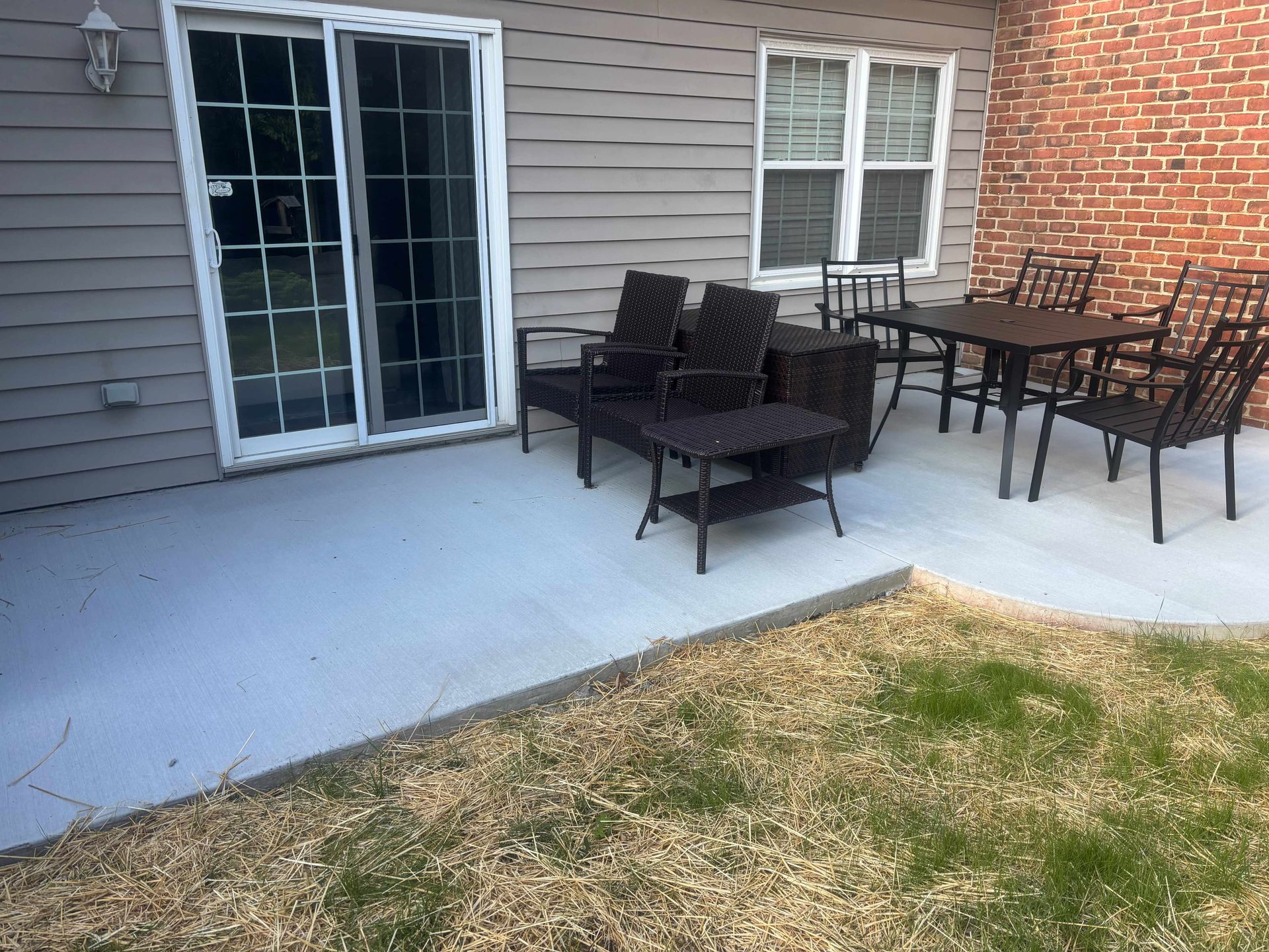 Patio with black outdoor seating beside sliding glass doors and a small grass patch nearby