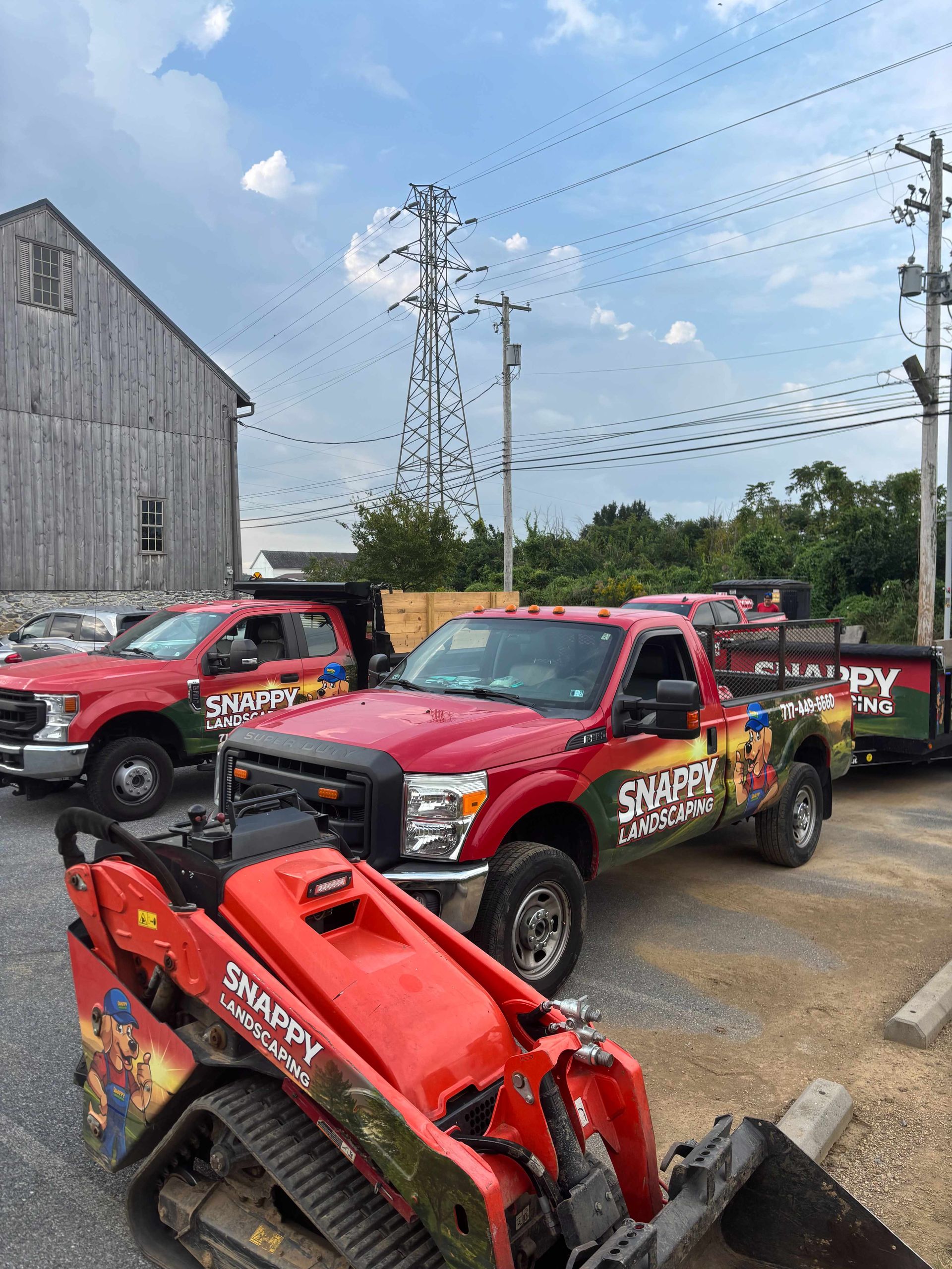 Red tow trucks lined up in a gravel lot beside a metal building and power lines.
