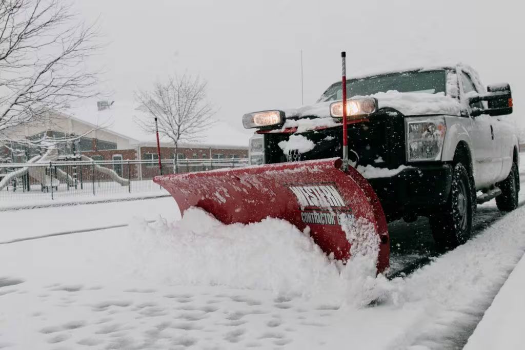 Snowplow clearing a street with a red blade in heavy snowfall