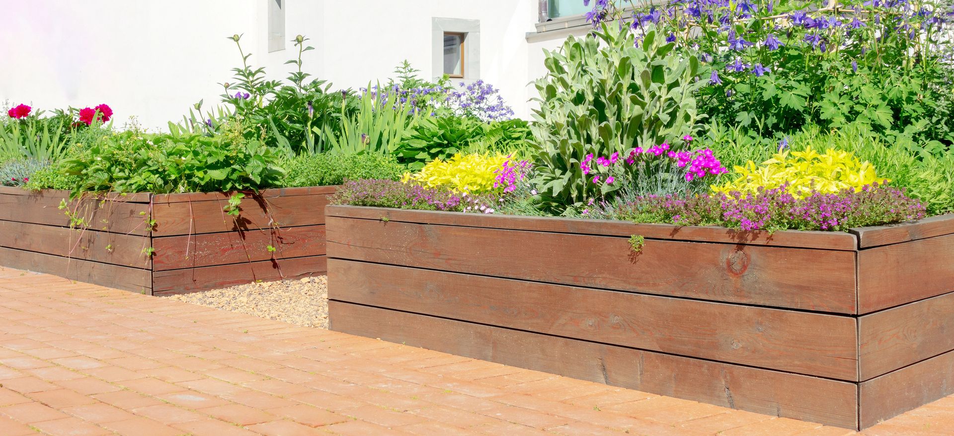 A wooden planter filled with flowers and plants in front of a house.
