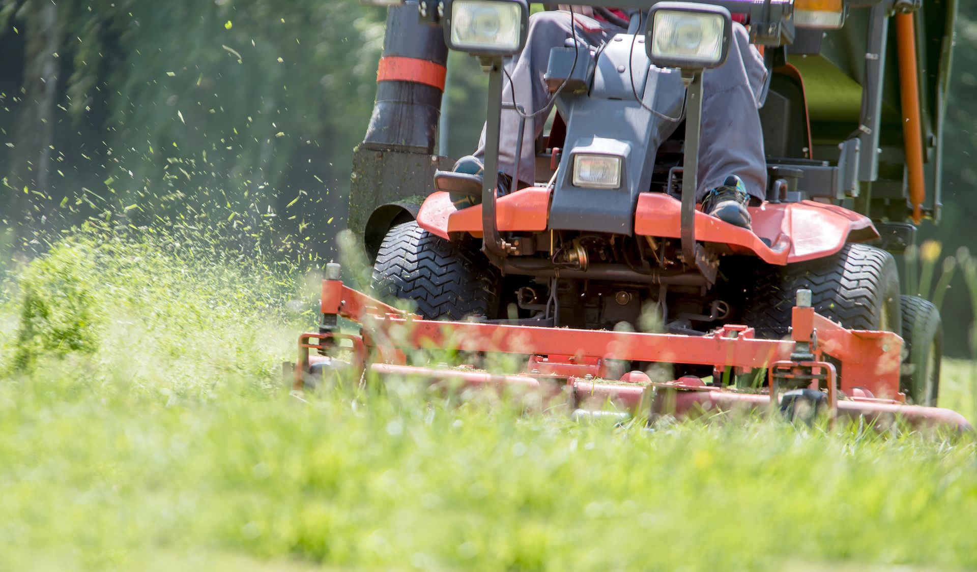 Red riding lawnmower mowing grass, with a person driving. Green grass and sunlight.