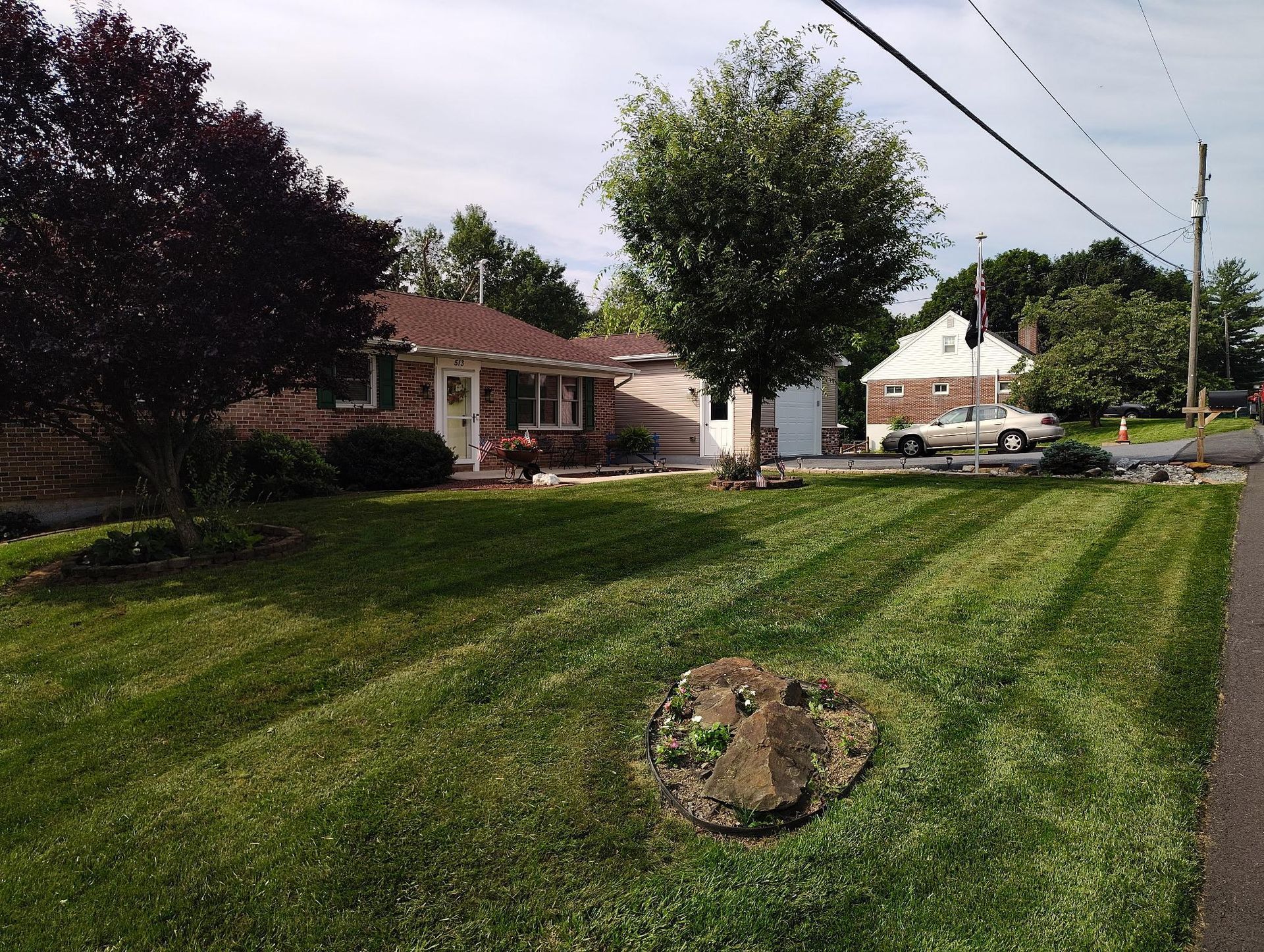 A residential house with a large lawn featuring striped mowing patterns, a mature tree, and a circular stone feature.
