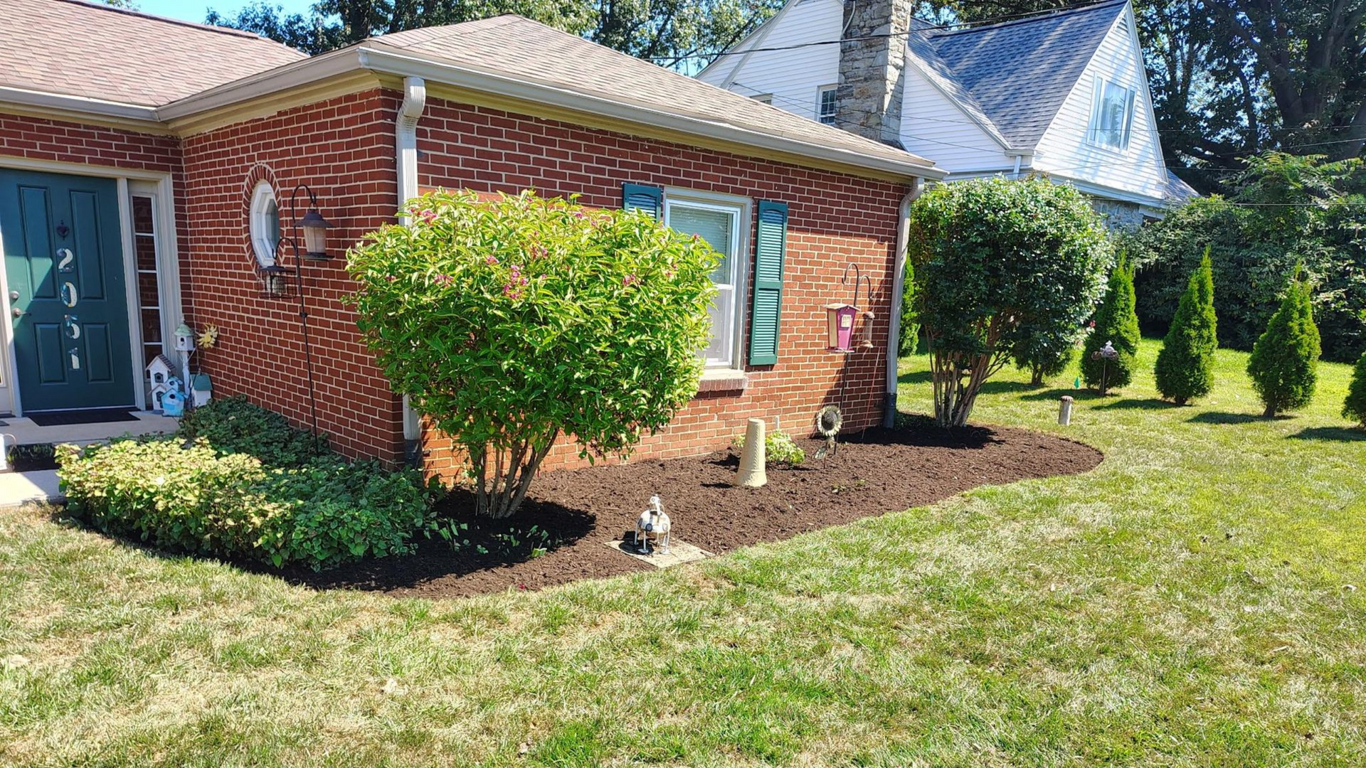 Brick house corner with trimmed shrubs and a green lawn under a bright sky