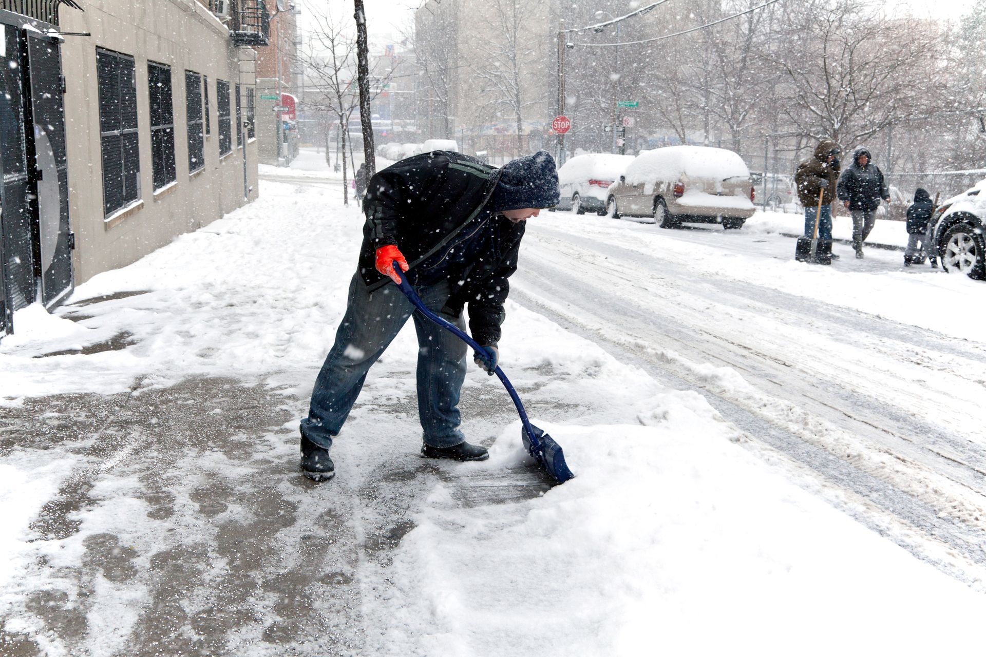 Person shoveling snow on a city sidewalk during a heavy snowfall