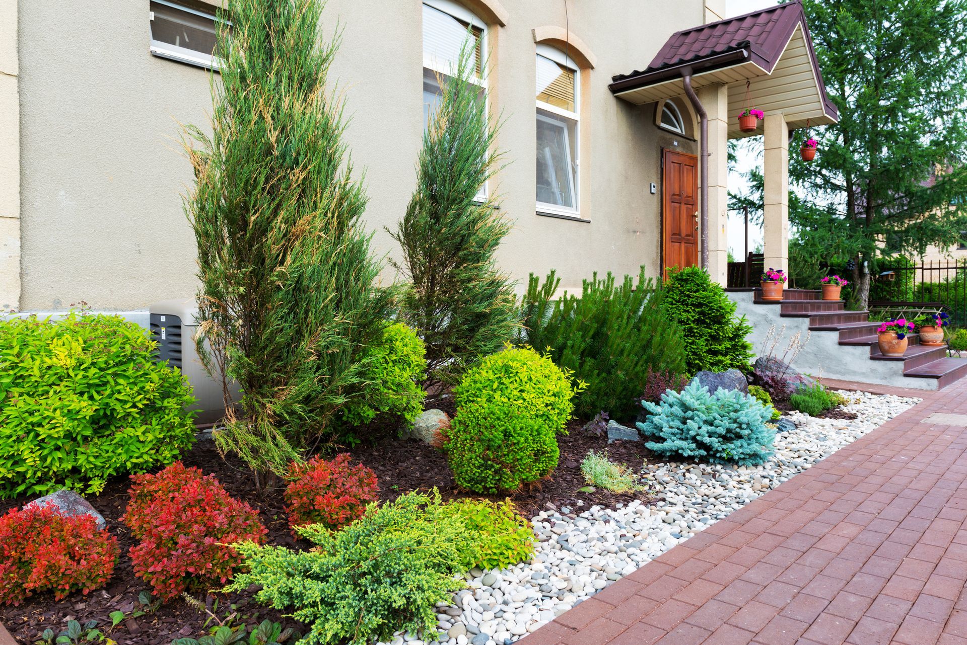 Landscaped front yard with colorful shrubs, white stones, and a brick walkway beside a house.