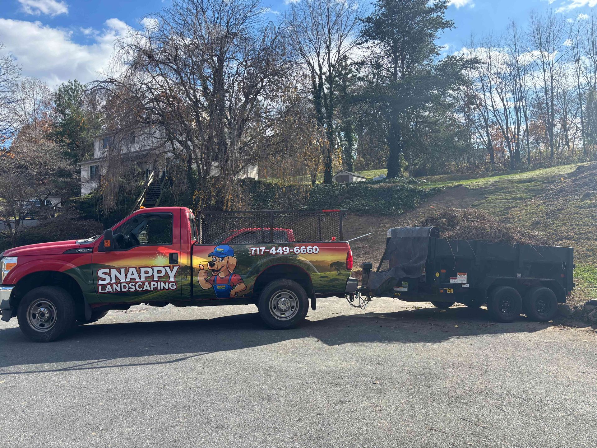 A red Snappy brand pickup truck pulling a dump trailer filled with yard debris, parked on an asphalt lot.