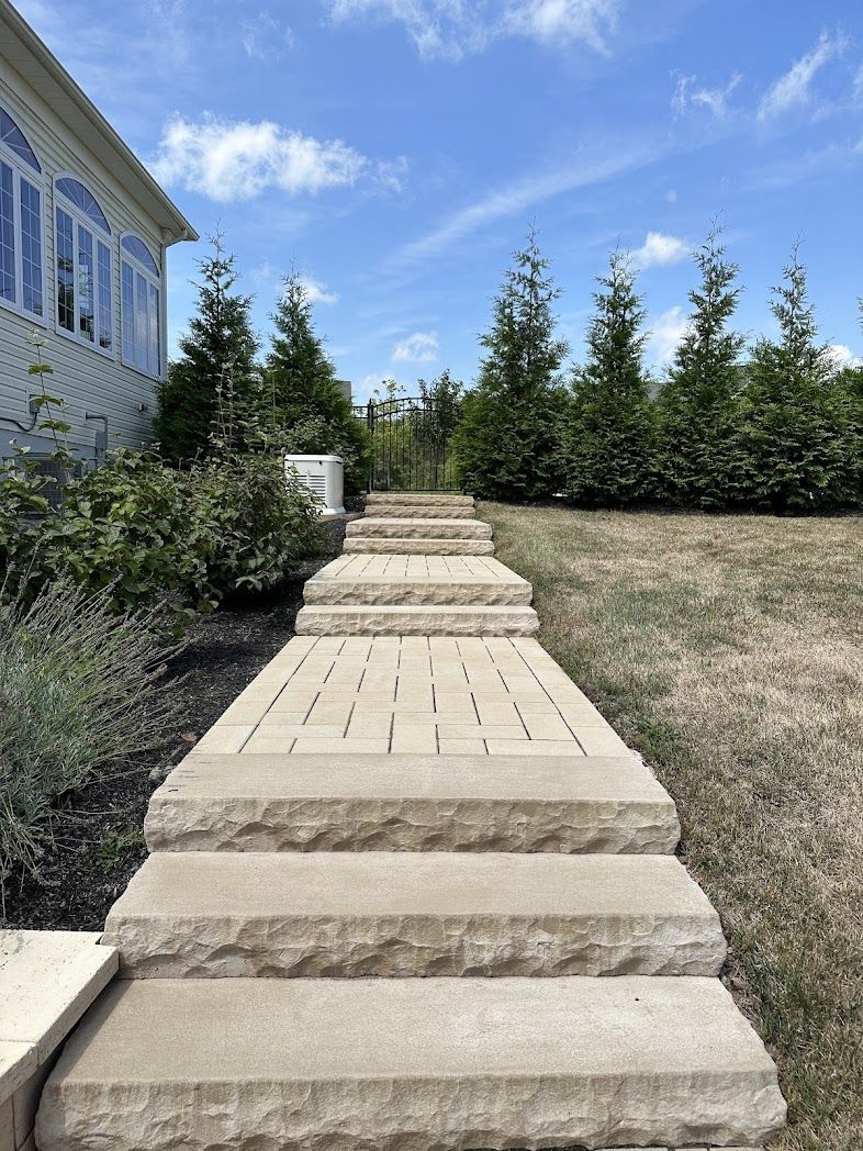 Stone steps lead up a landscaped yard beside a white house under a blue sky.