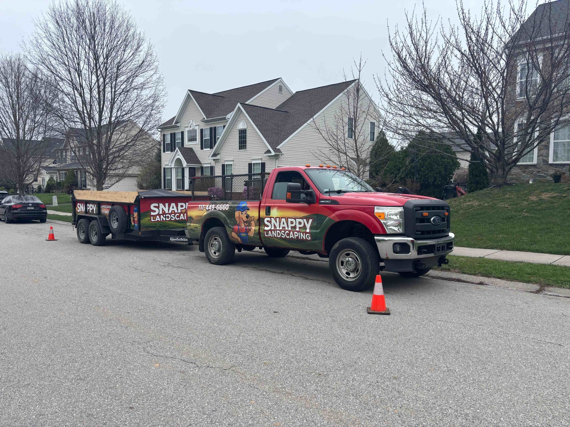 Red utility truck parked on a suburban street with road cones and side-panel advertising signage.