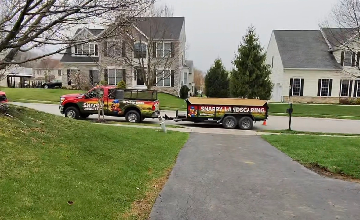 Red truck towing a trailer on a suburban street in front of houses on a cloudy day