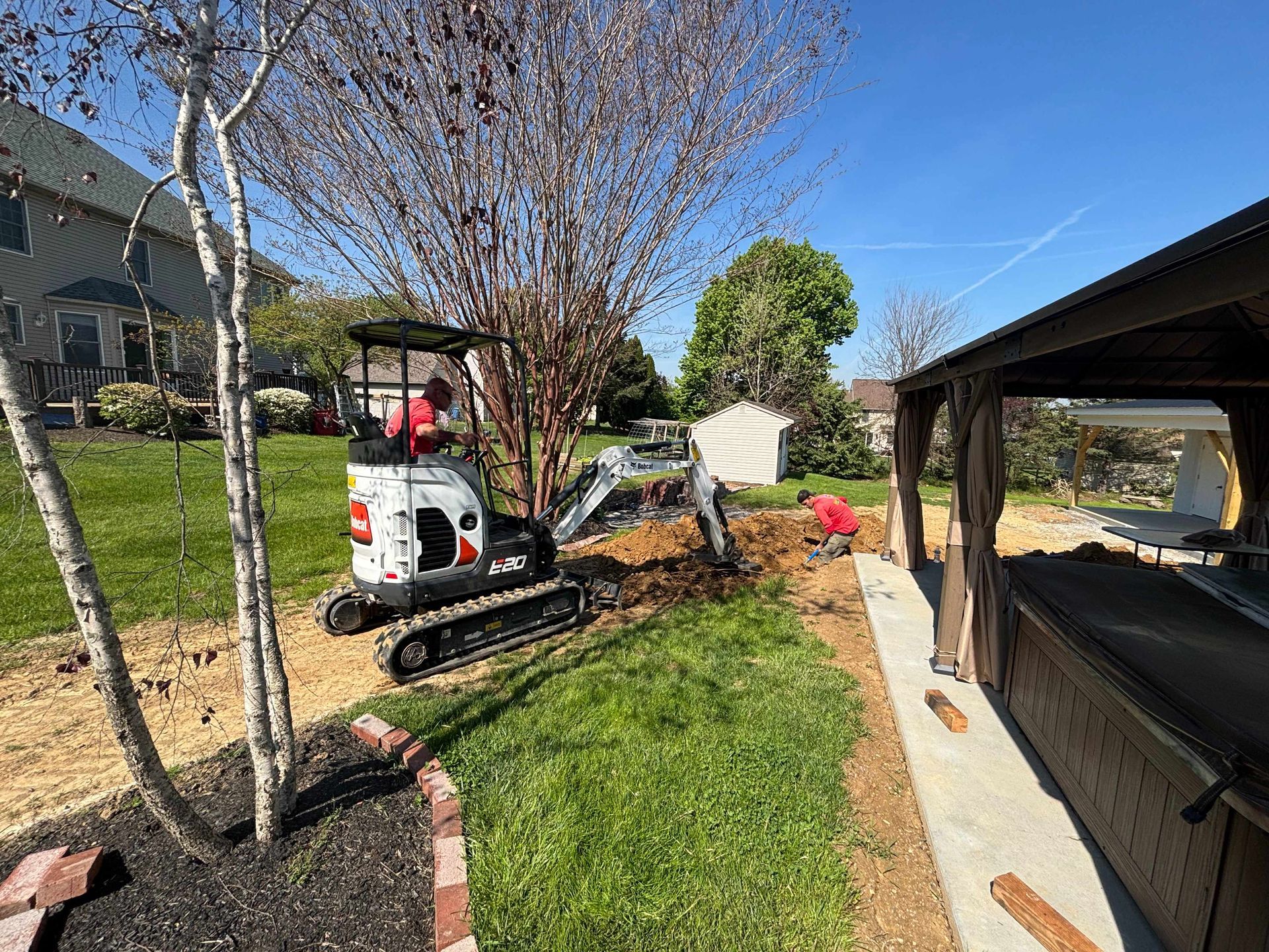 Mini excavator working in a landscaped yard beside a walkway and trees