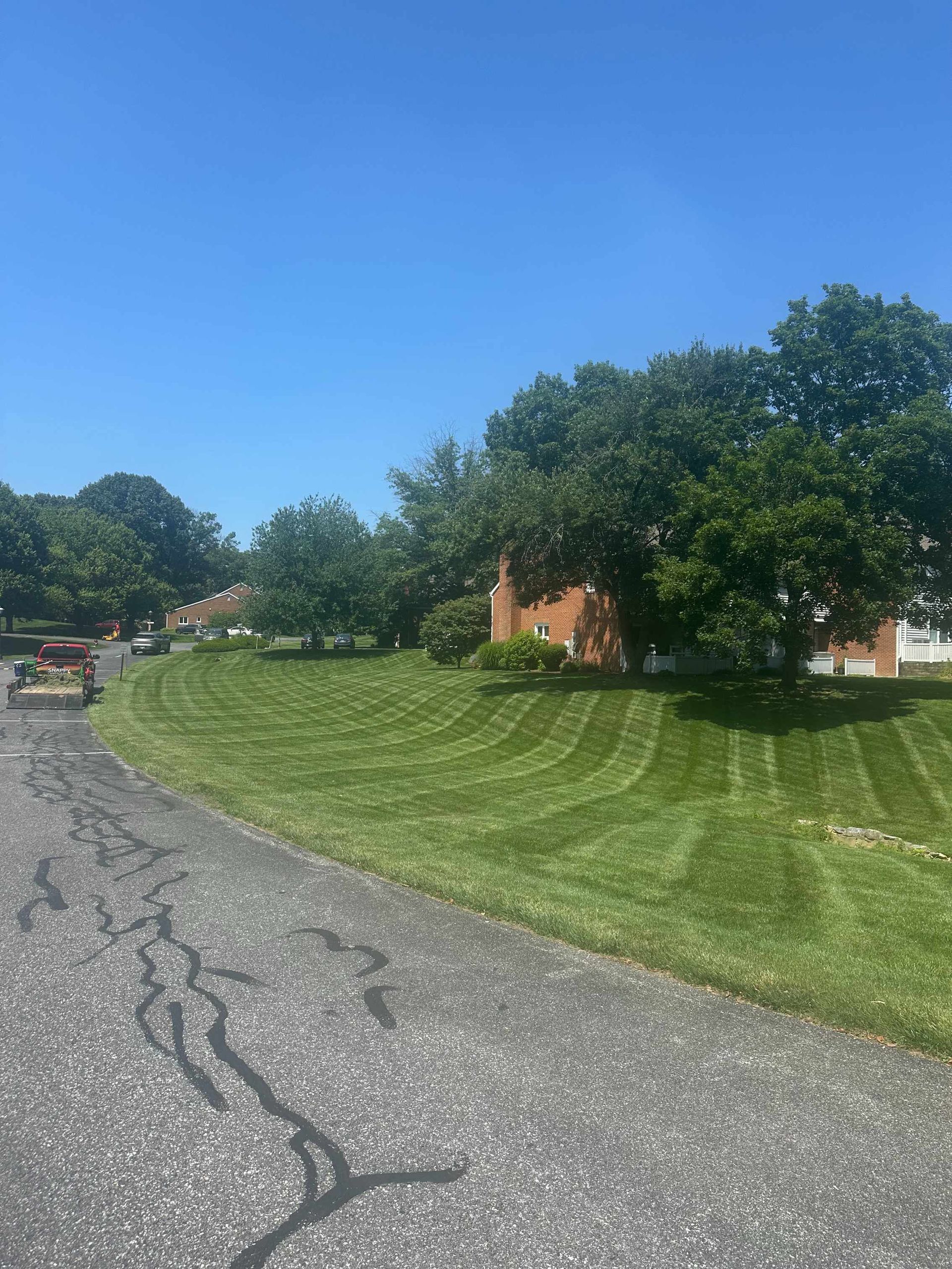 A freshly mowed, striped lawn curves alongside an asphalt road under a clear blue sky on a sunny day.