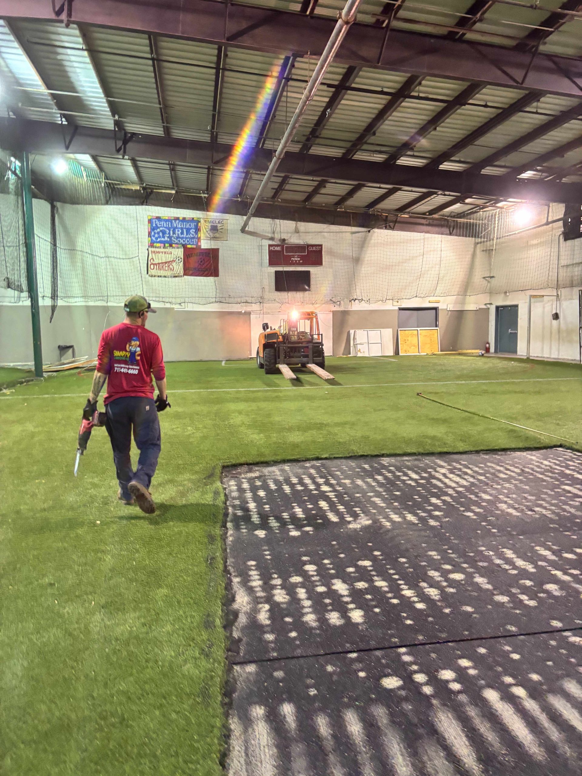 Indoor turf field with a person in a red shirt walking toward a small fire or smoke near the far wall