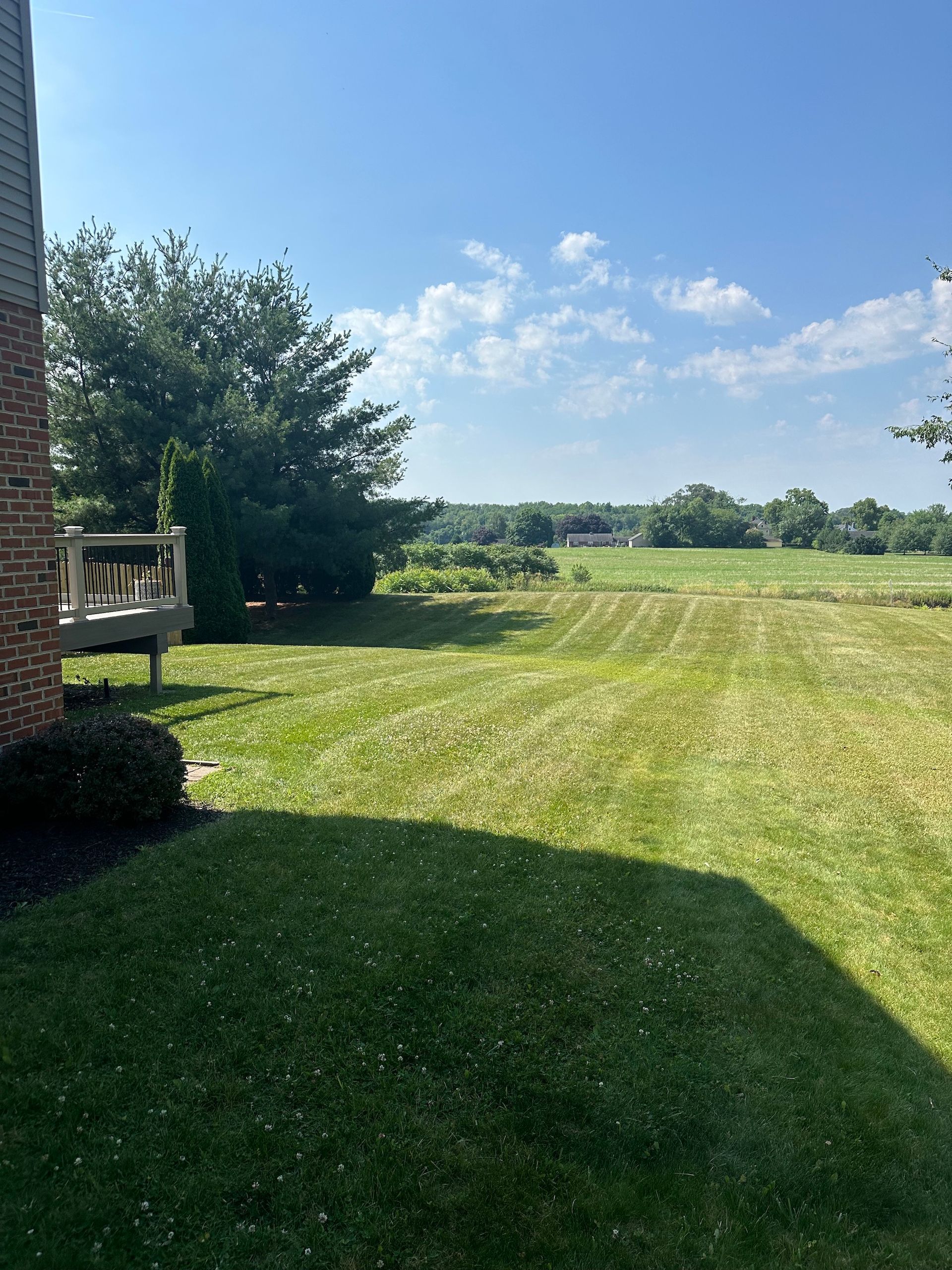 A lush green lawn with a brick building in the background and a large field in the background.