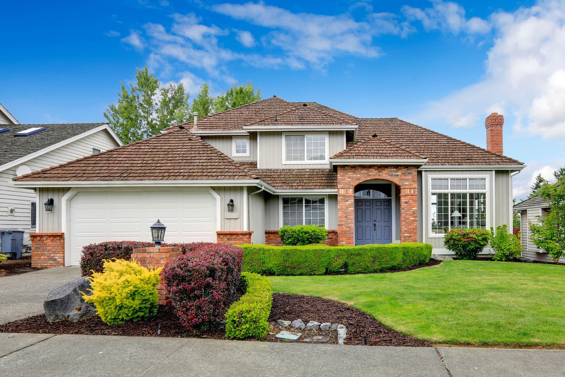 Single-story suburban house with tan stucco, red-tiled roof, trimmed shrubs, and a green lawn