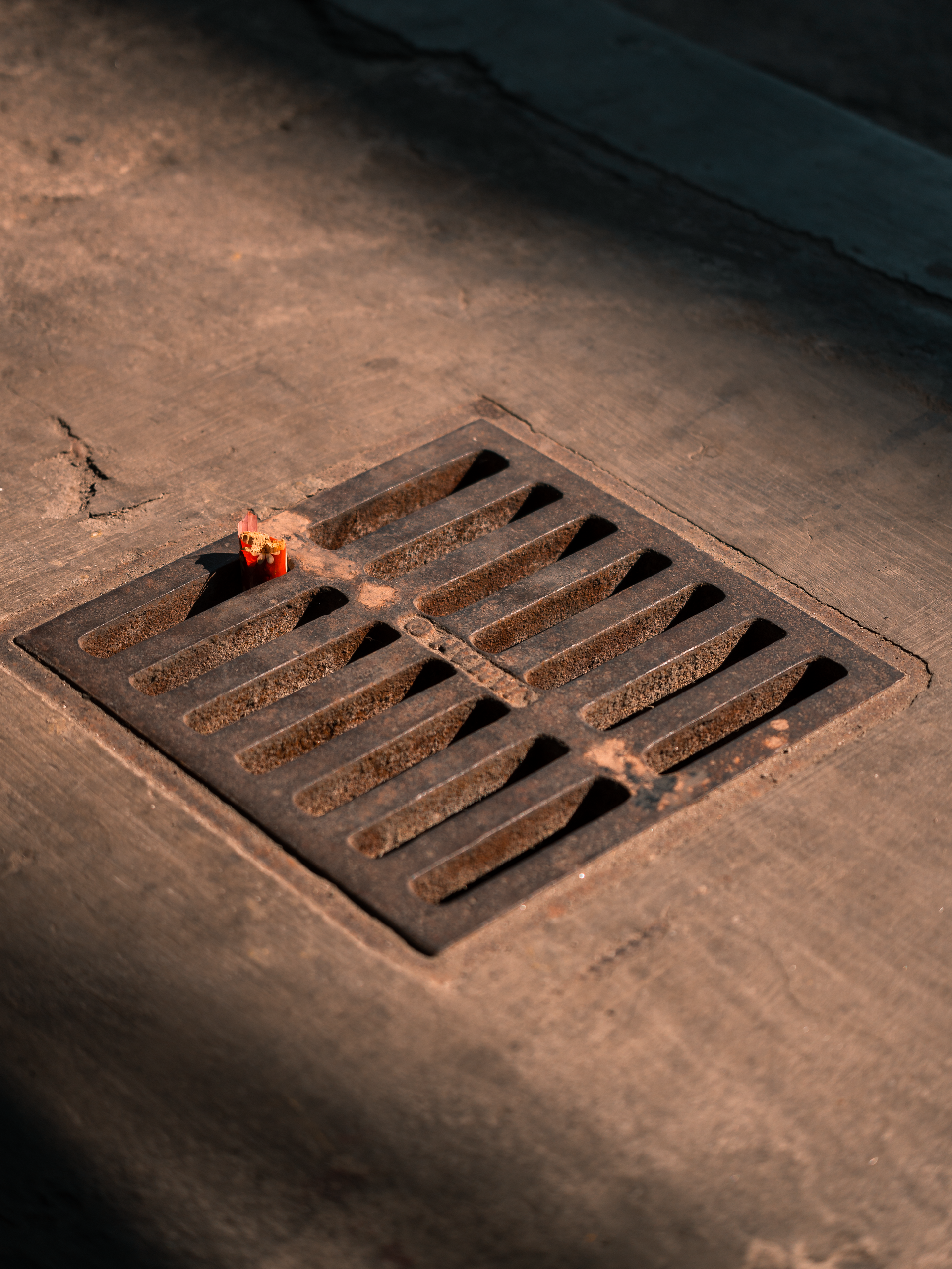 Small flame flickers beside a metal storm drain grate on a concrete pavement.