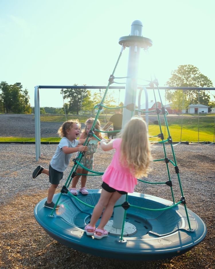 Three children playing on a spinning playground climber at sunset
