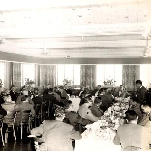 Black-and-white banquet in a dining hall, with many people seated at long tables under fluorescent lights