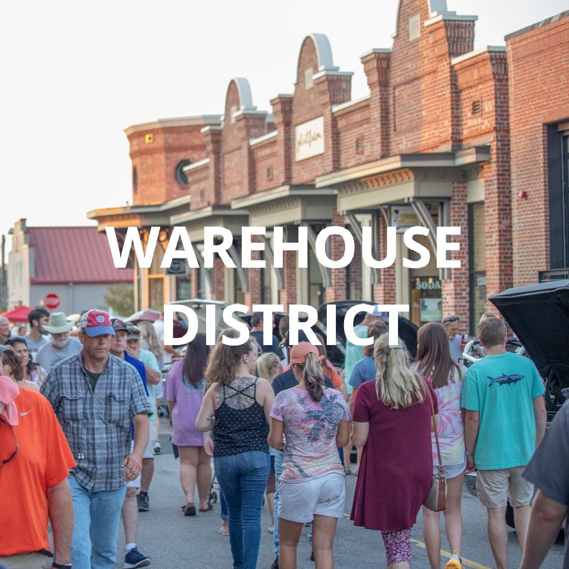 Crowd walking in a brick-lined street under a sign reading “Warehouse District”