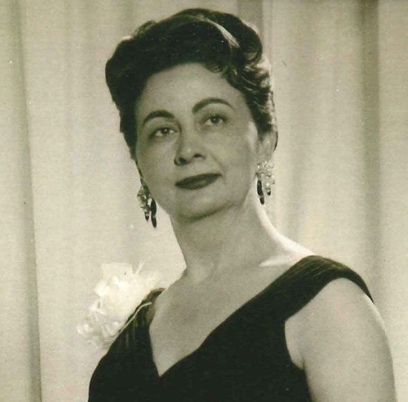 Formal portrait of a woman in a black dress with a white corsage, posed before a curtain backdrop